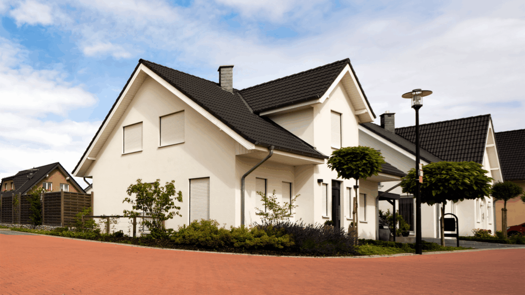 A modern suburban house with white walls and a dark roof on a quiet street, showcasing recent stucco repair under a clear blue sky.